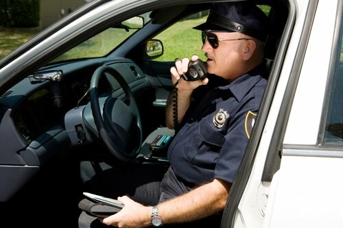 Police officer using radio in patrol car.